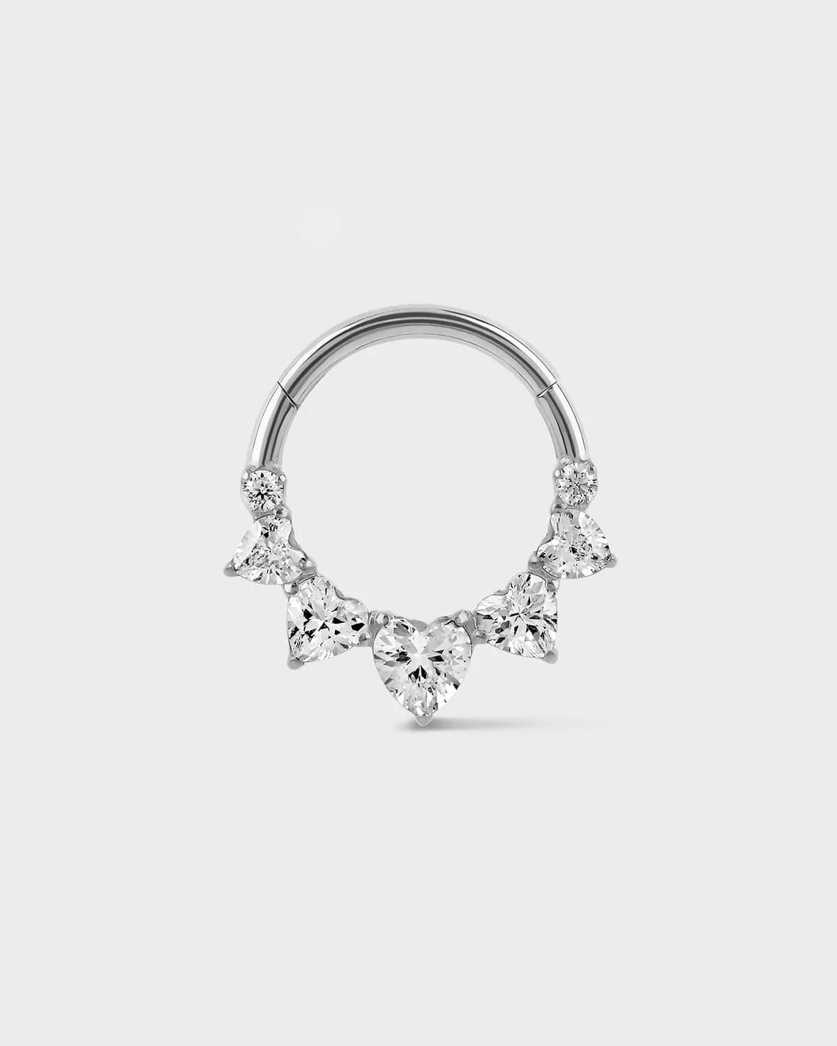 Polished titanium Daith or septum ring with five graduated heart shape gems and two smaller round gem sat on a light gray background