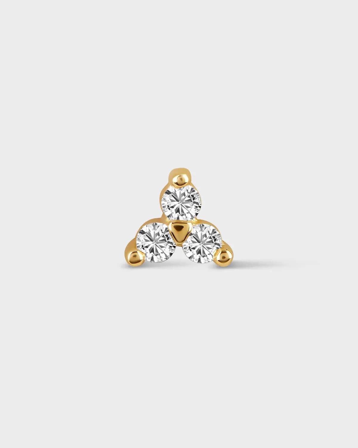 Gold earring with three clear gemstones on a light gray background