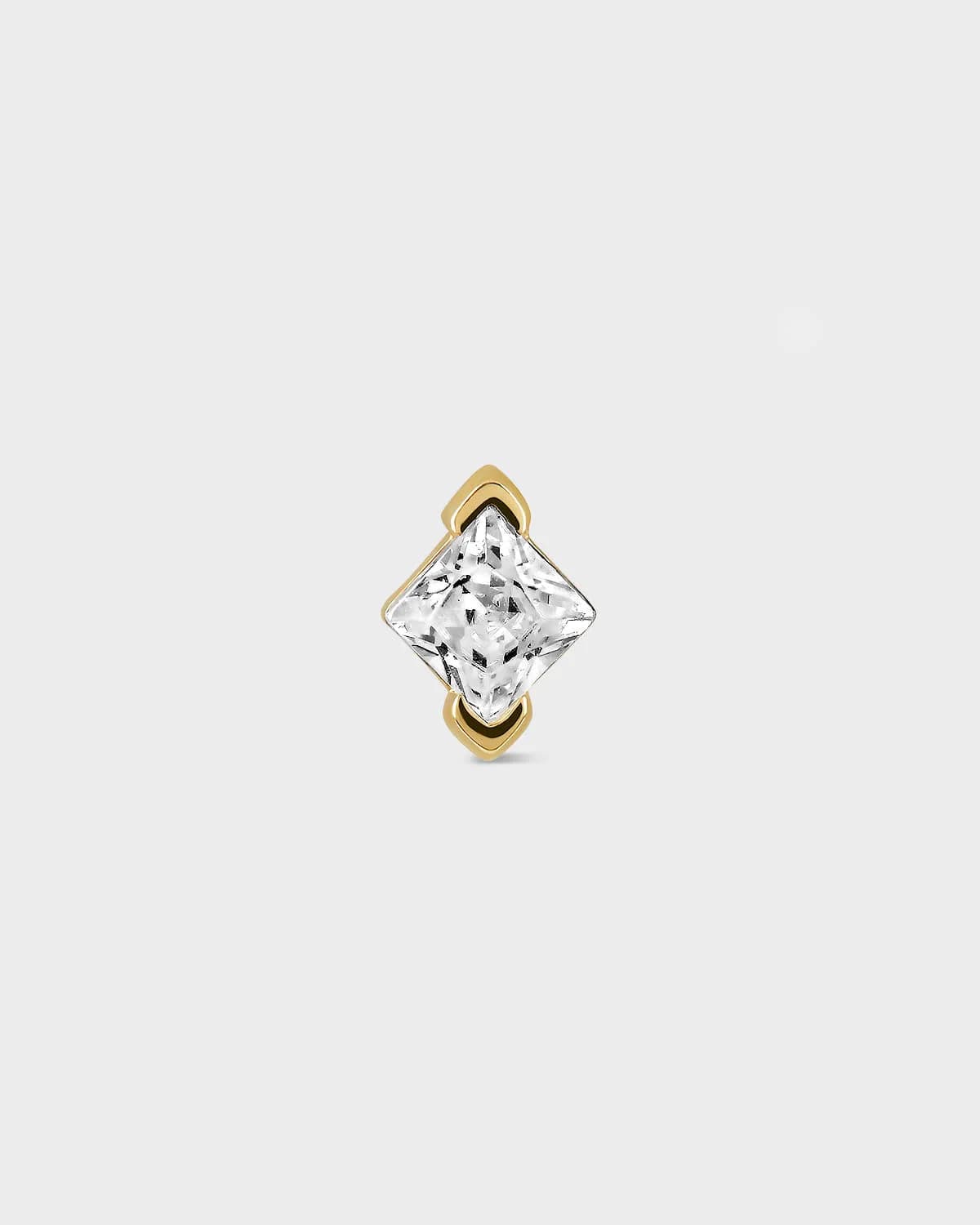 Gold earring with a clear gemstone on a light gray background