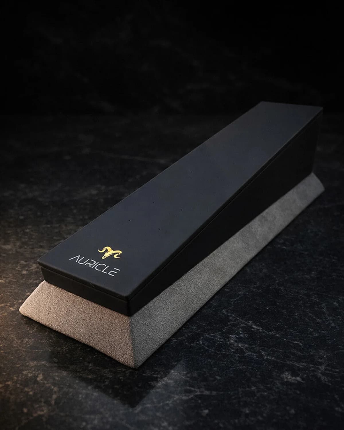 jewellery display stand to hold 20 pieces of jewellery. The stand has a light gray suede base with a black leather top. Sat on a dark worktop with moody lighting.