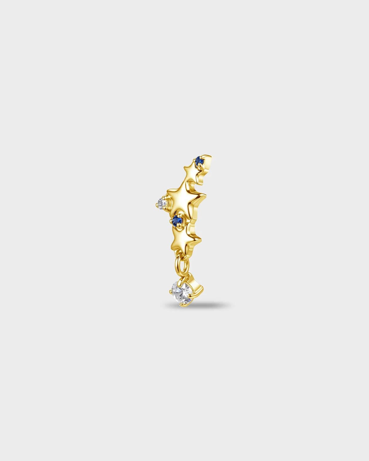 Gold titanium earring with a row of star shapes set with blue and clear round-cut stones, finished with a short dangle and a clear round-cut stone, on a light gray background.
