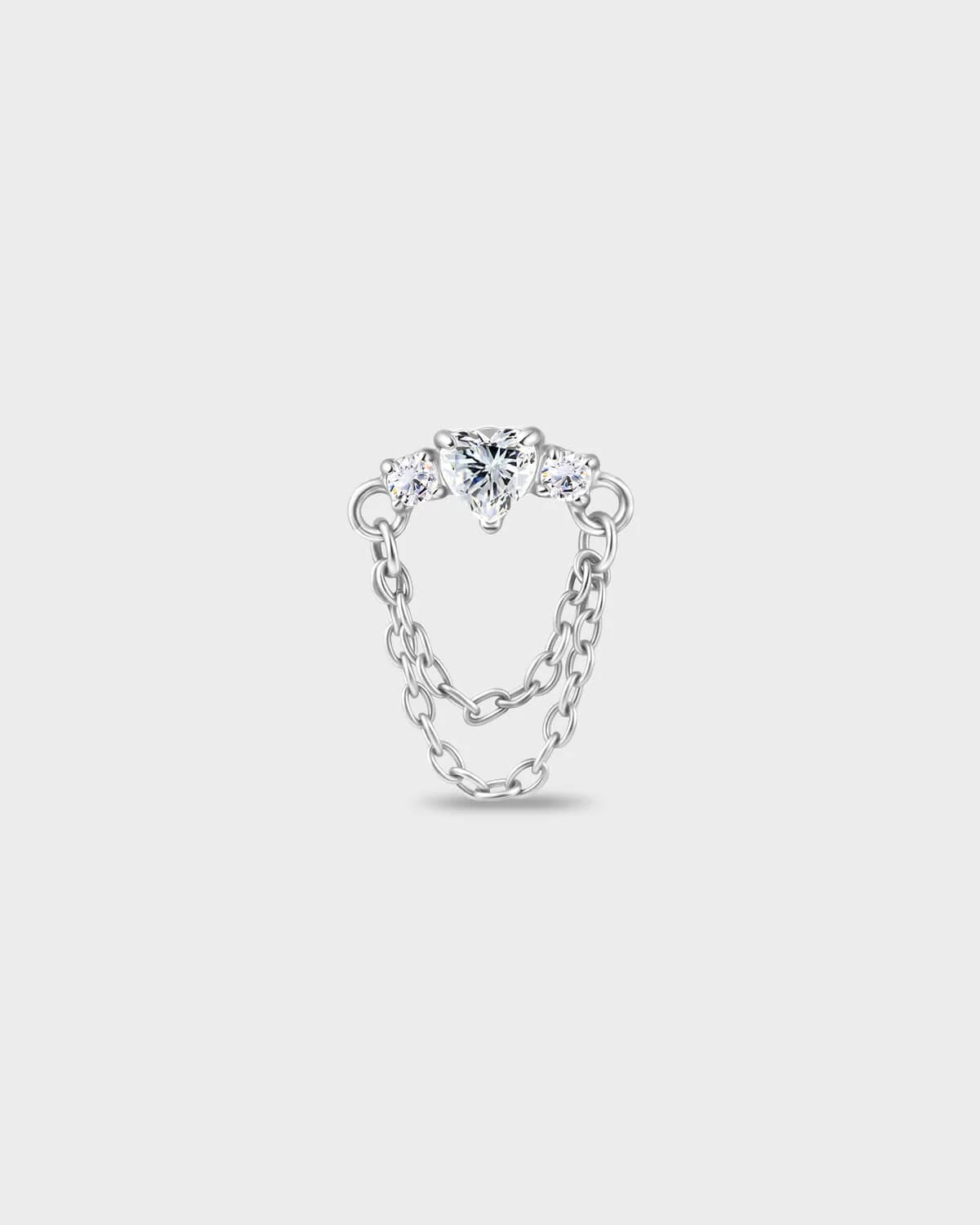 Polished titanium earring with a heart-cut clear stone set between two smaller round-cut stones, finished with a double chain detail on a light gray background.