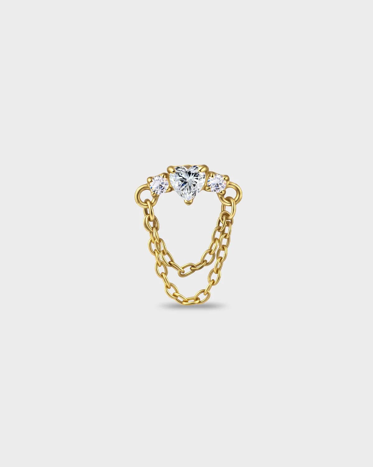 Gold titanium earring with a heart-cut clear stone set between two smaller round-cut stones, finished with a double chain detail on a light gray background.
