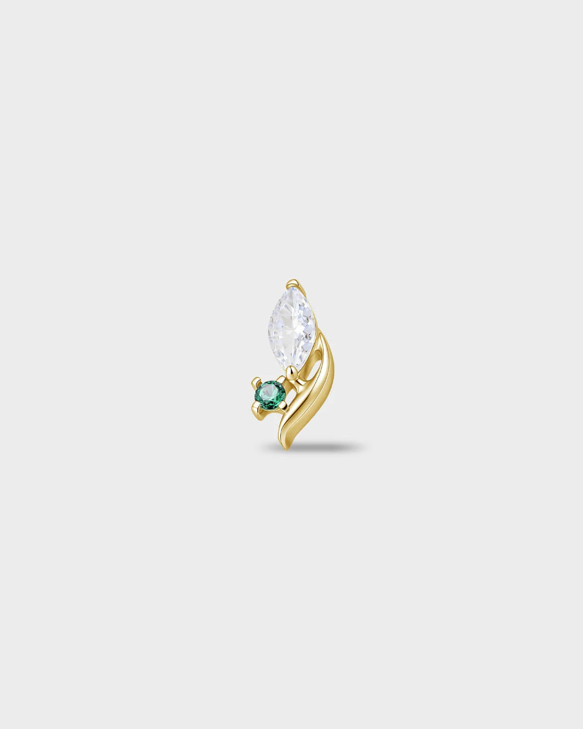 Gold titanium earring with a marquise-cut clear stone and a small round-cut emerald green stone set on a curved base, on a light gray background.