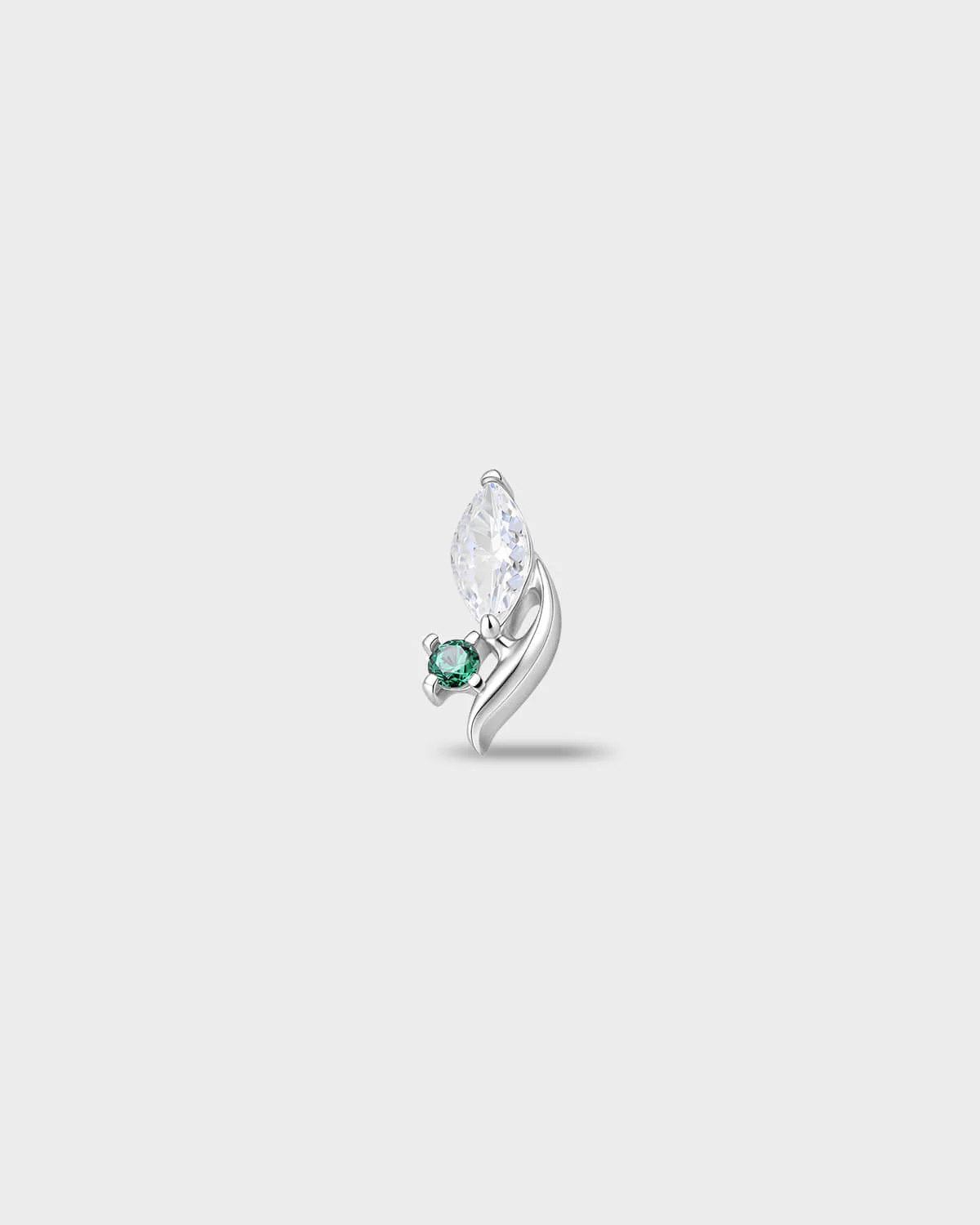 Polished titanium earring with a marquise-cut clear stone and a small round-cut emerald green stone set on a curved base, on a light gray background.